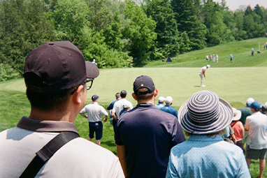 Spectators watch a golfer on a sunny day.