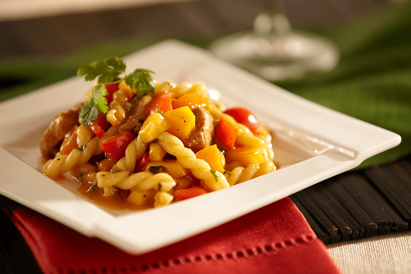 Plate of gemelli pasta with colorful bell peppers and herbs, topped with parsley. Set on red napkin, creating a warm, inviting atmosphere.